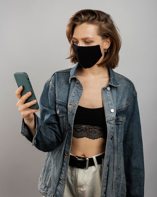 Gratis foto vrouw denim jasje en masker dragen tijdens het gebruik van mobiel