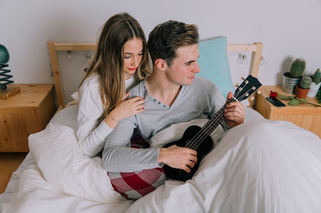 Gratis foto vrouw dichtbij man het spelen ukelele in bed