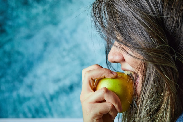 Vrouw die appel op blauwe muur eet.