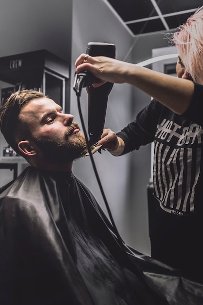 Vrouw die baard van cliënt kamt en droogt