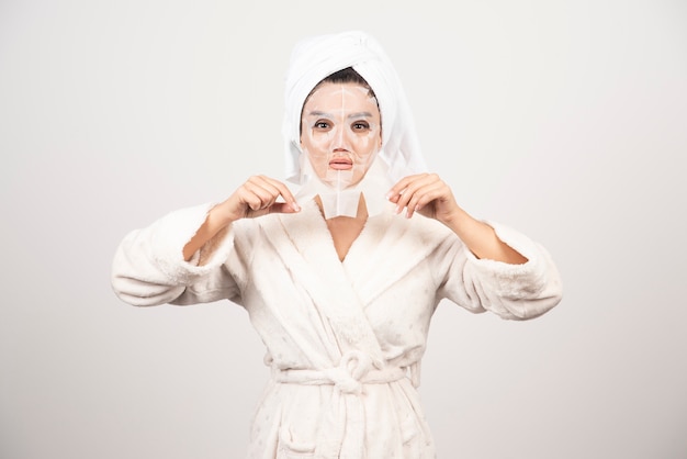 Vrouw die badjas en handdoek met gezichtsmasker draagt.