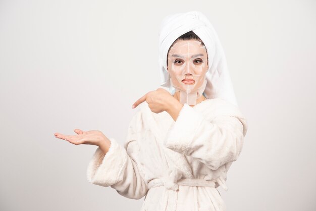 Vrouw die badjas en handdoek met gezichtsmasker draagt
