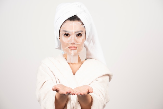 Vrouw die badjas en handdoek met gezichtsmasker draagt