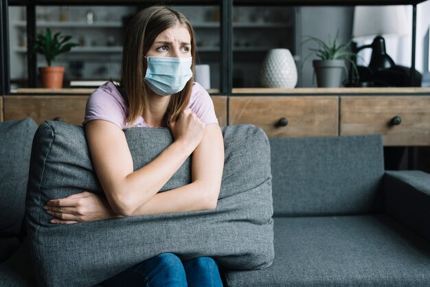 Vrouw die beschermende maskerzitting op bank draagt