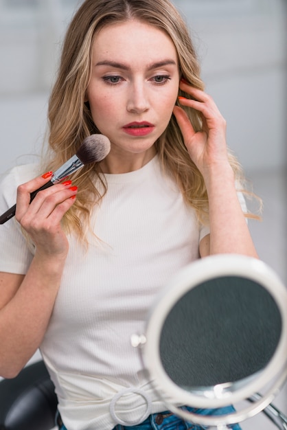 Gratis foto vrouw die blusher toepast die in spiegel kijkt