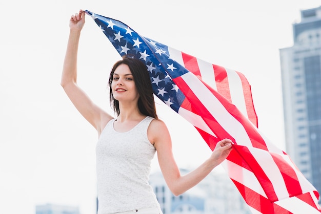 Vrouw die camera bekijkt en Amerikaanse vlag golft