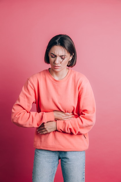 Gratis foto vrouw die casual trui draagt op achtergrond die buikpijn met pijnlijke grimas lijdt, plotselinge menstruatiekrampen, gynaecologieconcept voelt