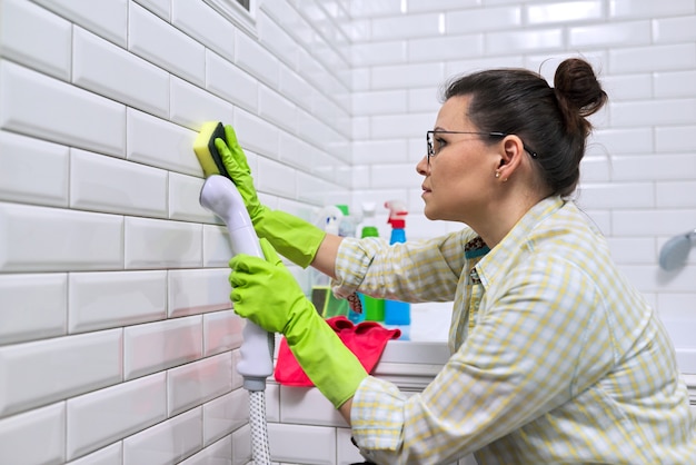 Vrouw die de badkamer thuis schoonmaakt, de vrouwelijke wastegelmuur met stoom stoomreiniger gebruiken voor snelle reiniging
