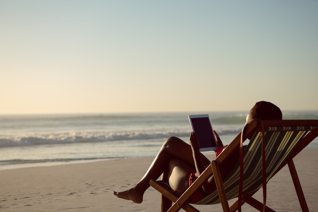Vrouw die digitale tablet gebruiken terwijl het ontspannen in een ligstoel op het strand