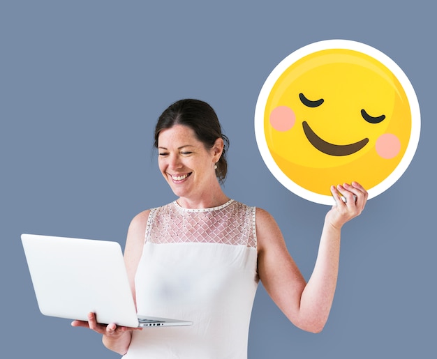 Gratis foto vrouw die een blozende emoticon houdt en laptop met behulp van