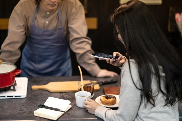 Vrouw die een foto neemt van een kopje koffie en een donut in een restaurant