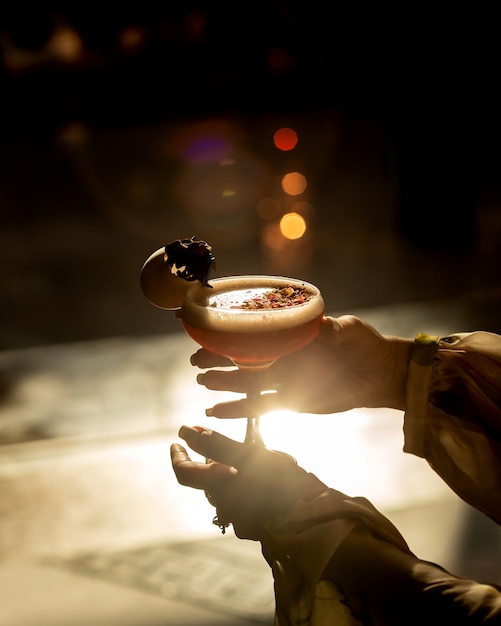 Vrouw die een glas cocktail in zonsondergang houdt