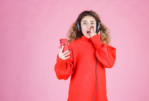 vrouw die een koptelefoon draagt en naar haar afspeellijst luistert op smartphone en ziet er ontevreden uit.