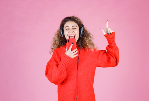 vrouw die een koptelefoon draagt, luistert naar haar afspeellijst op smartphone en danst.