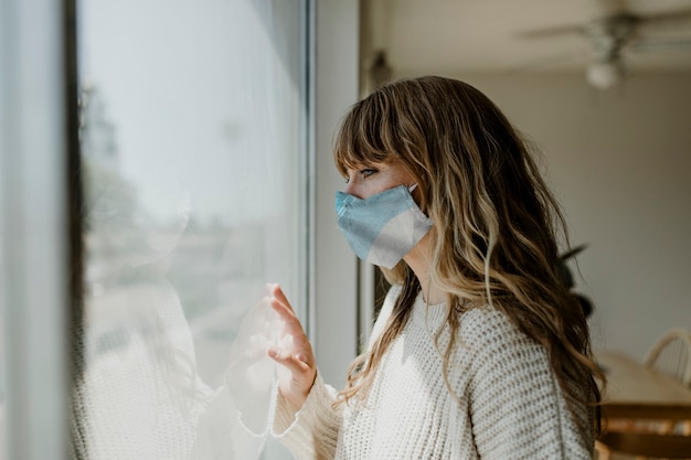 Vrouw die een masker draagt en uit het raam staart tijdens een lockdown