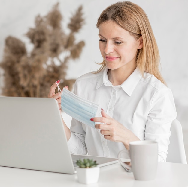 Vrouw die een medisch masker voor haar laptop camera houdt