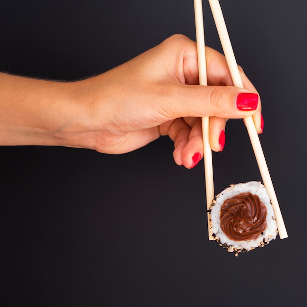 Vrouw die een paar eetstokjes met een sushibroodje houdt op een zwarte achtergrond