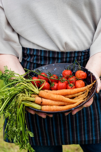 Vrouw die een plaat van wortelen en tomaten houdt