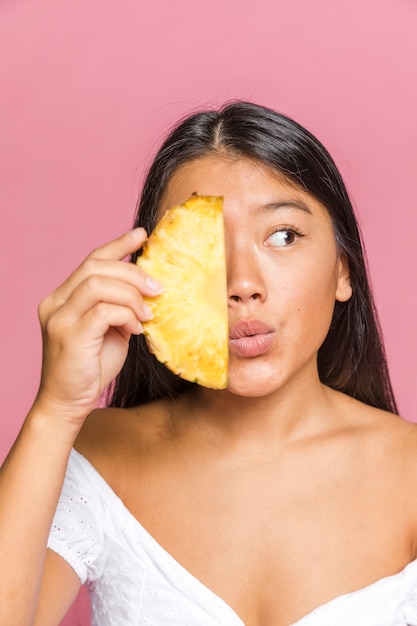 Vrouw die een plak van ananas houdt en weg kijkt