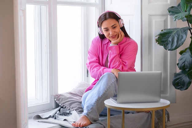 Vrouw die een videogesprek voert op een laptop terwijl ze thuis op de vensterbank zit