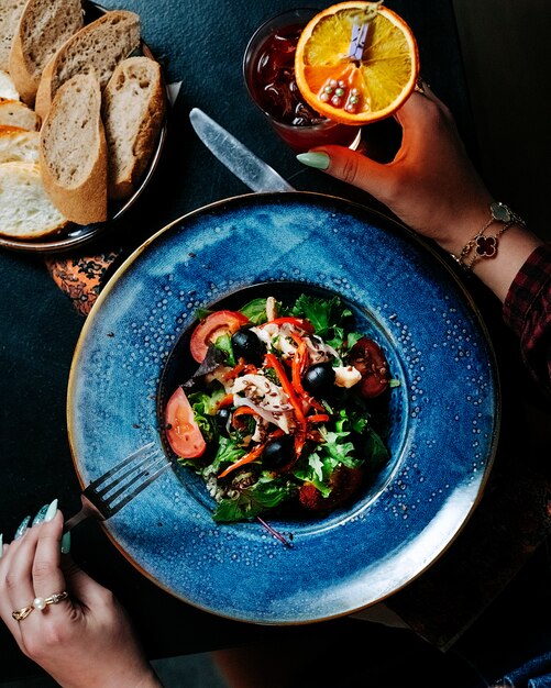 Vrouw die een vork zet om gemengde seizoengebonden plantaardige salade binnen blauwe plaat te eten.