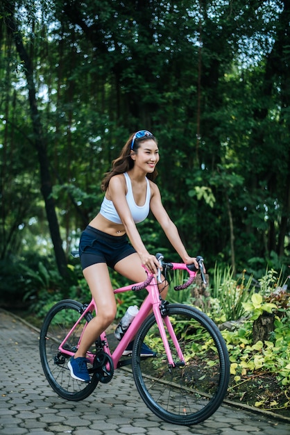 Vrouw die een wegfiets in het park berijdt. Portret van jonge mooie vrouw op roze fiets.