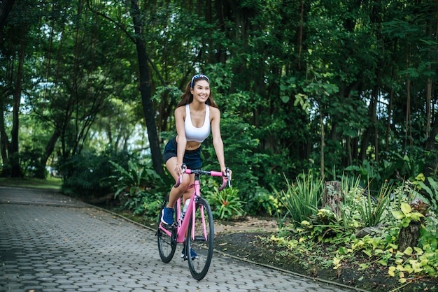 Vrouw die een wegfiets in het park berijdt. Portret van jonge mooie vrouw op roze fiets.