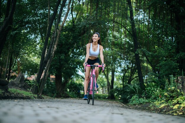 Vrouw die een wegfiets in het park berijdt. Portret van jonge mooie vrouw op roze fiets.