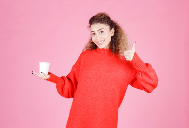 Vrouw die een wegwerpkoffiekopje vasthoudt en geniet van de smaak.