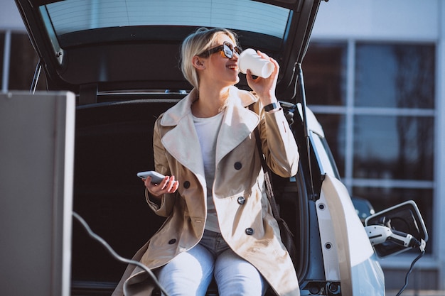 Vrouw die elektrocar laadt bij het elektrische benzinestation