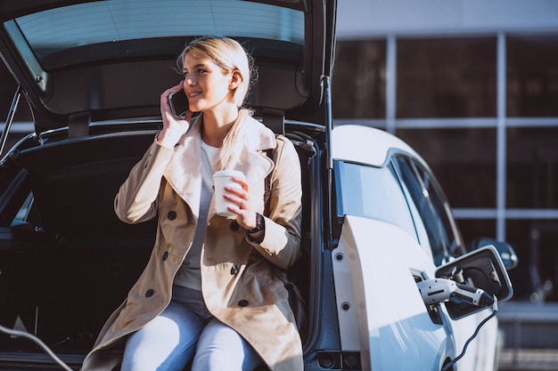 Vrouw die elektrocar laadt bij het elektrische benzinestation