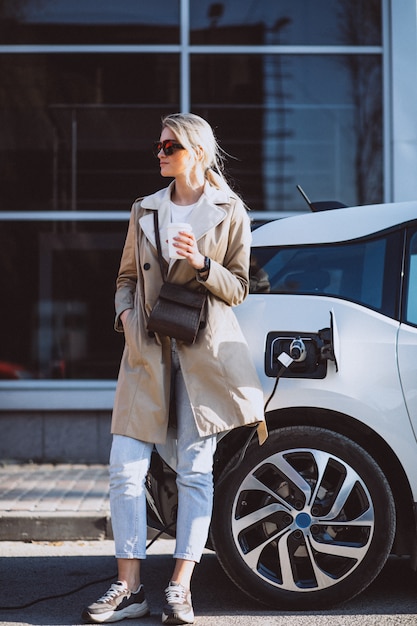 Vrouw die elektrocar laadt bij het elektrische benzinestation