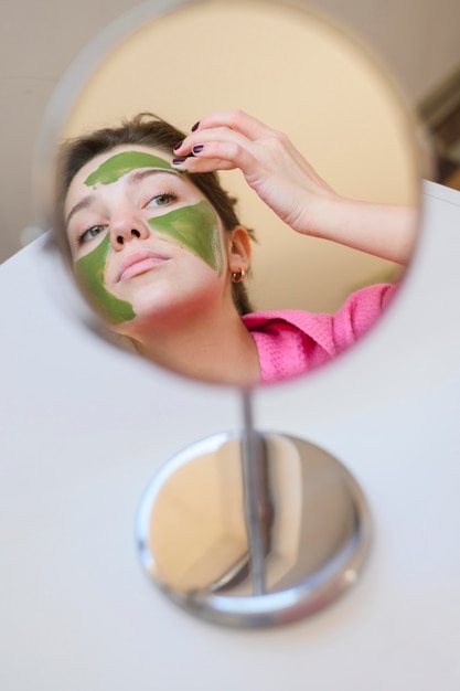 Gratis foto vrouw die gezichtsmasker in de spiegel toepast