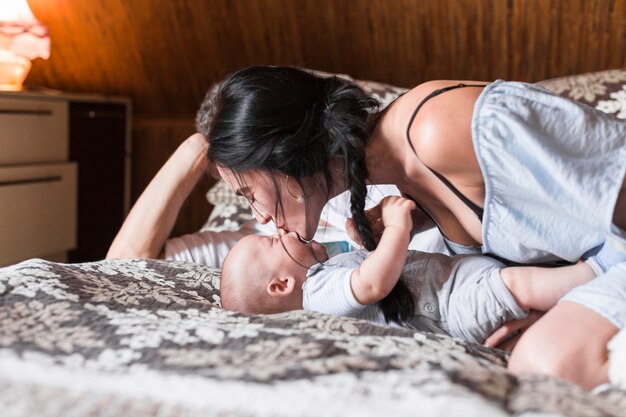 Vrouw die haar baby kust die op bed in de slaapkamer ligt