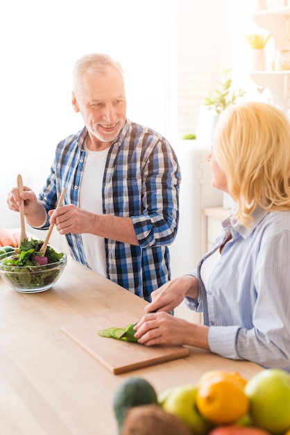 Vrouw die haar echtgenoot bekijkt die de salade in de keuken voorbereidt