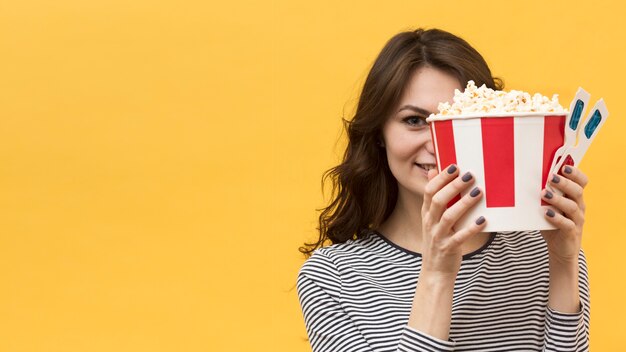 Vrouw die haar gezicht behandelt met 3d glazen en emmer met popcorn