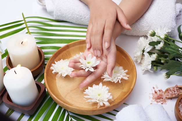 Vrouw die haar handen in een kom met water en bloemen drenkt, kuur en product voor vrouwelijke voeten en handkuuroord, massagekiezel, geparfumeerd bloemenwater en kaarsen, ontspanning. Plat leggen. bovenaanzicht.