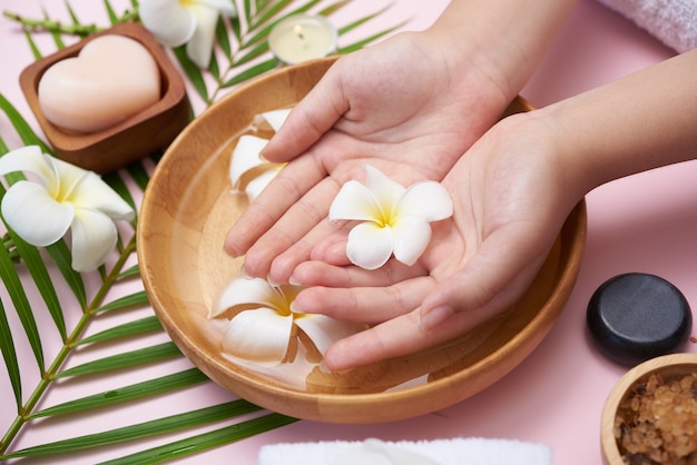 Vrouw die haar handen in een kom met water en bloemen drenkt, kuur en product voor vrouwelijke voeten en handkuuroord, massagekiezel, geparfumeerd bloemenwater en kaarsen, ontspanning. Plat leggen. bovenaanzicht.