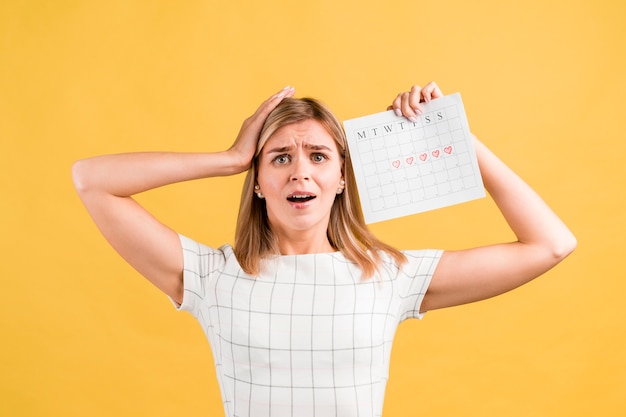 Vrouw die haar handen op haar hoofd en periodekalender zet