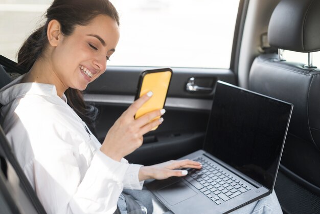 Vrouw die haar mobiele telefoon en laptop in de auto gebruiken