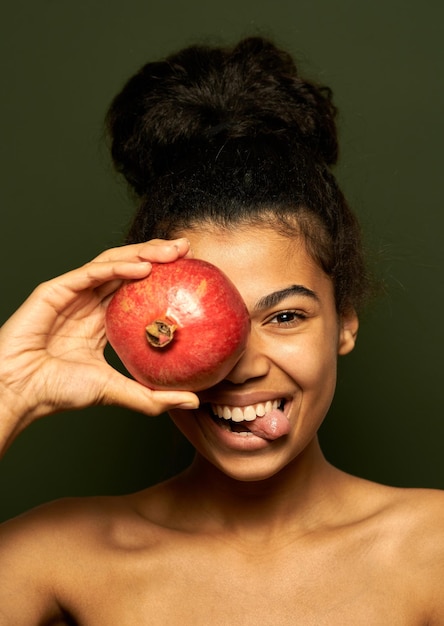 vrouw die haar tong laat zien, granaatappelfruit op haar oog houdt, geïsoleerd op groen