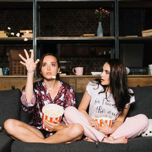 Vrouw die haar vrouwelijke vriend bekijkt die popcorn werpt terwijl het letten van op film