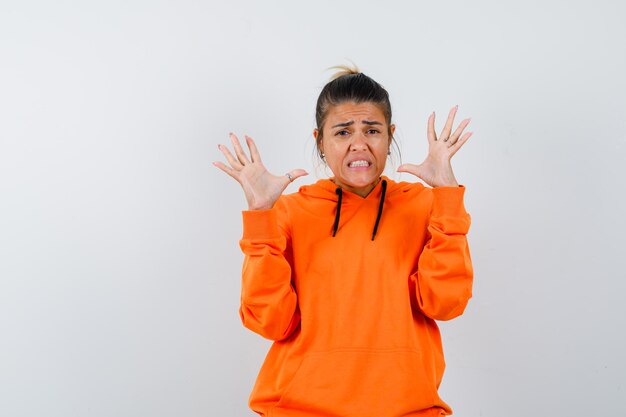 vrouw die handen op een agressieve manier opsteekt in oranje hoodie en er walgelijk uitziet