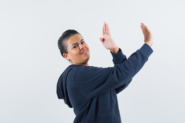 Vrouw die handen opheft om zich in hoodie te verdedigen en er zelfverzekerd uitziet.