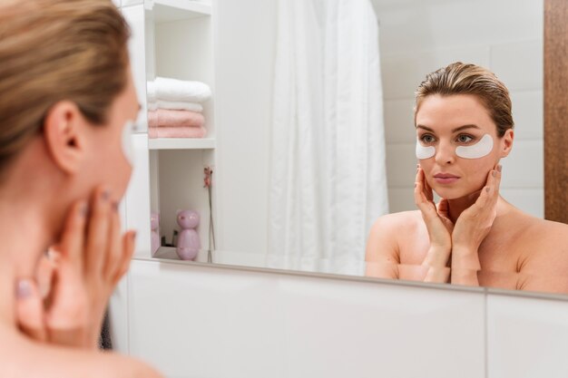 Vrouw die het verminderen van donkere kringenvlekken in de spiegel gebruikt