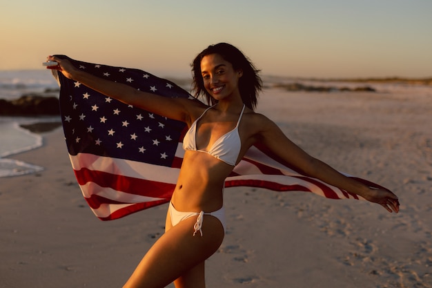 Vrouw die in bikini een amerikaanse vlag op het strand houdt