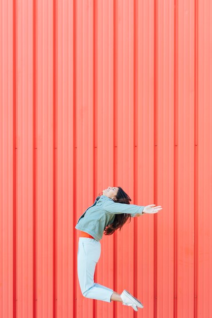 Vrouw die in de lucht tegen rood metaal golft geweven achtergrond springt