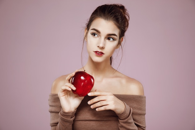 vrouw die in kant kijkt die rode appel op roze houdt