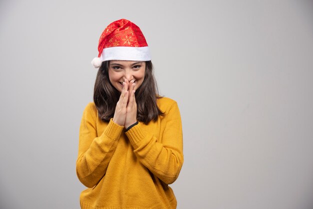 Vrouw die in Kerstmanhoed stil op grijze muur lacht.