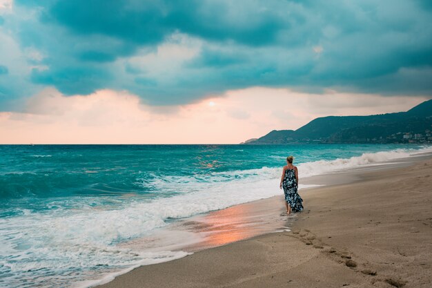 Vrouw die in lange kleding aan kust loopt